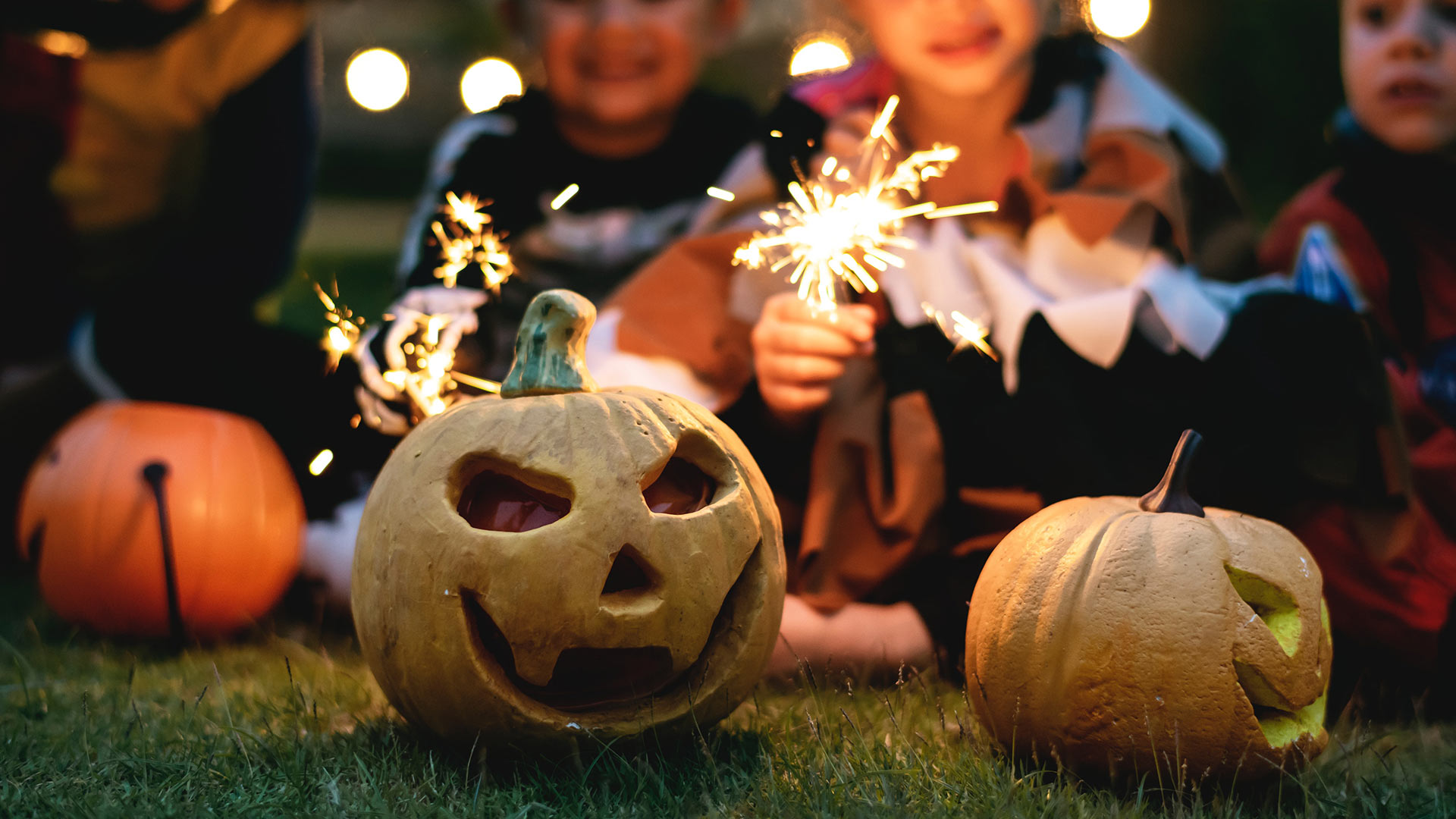 Carved pumpkins for Halloween with children holding sparklers in background